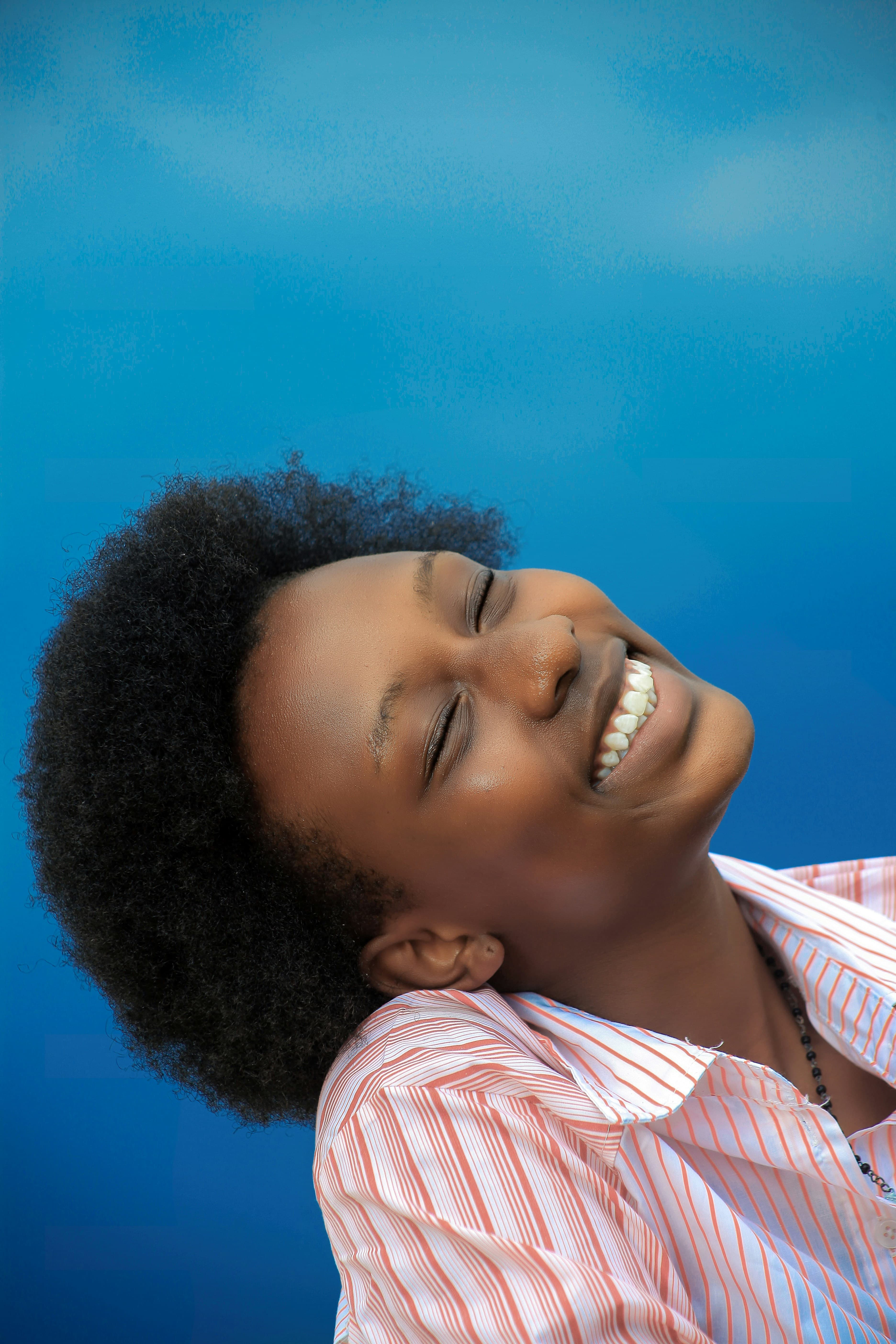 A young woman laughing with her head tilted back against a clear blue sky