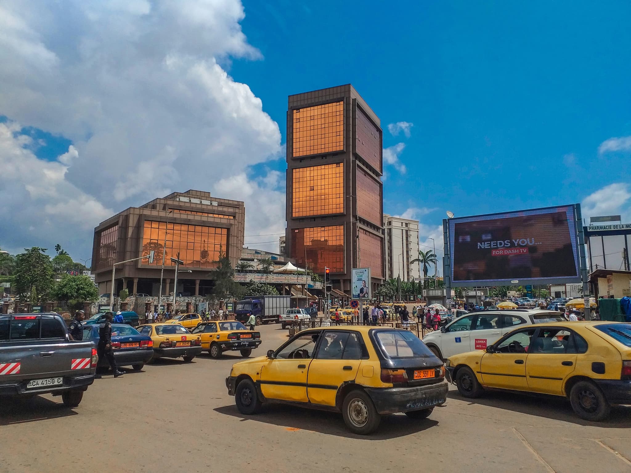A busy market street, traders and yellow shared taxis packed together