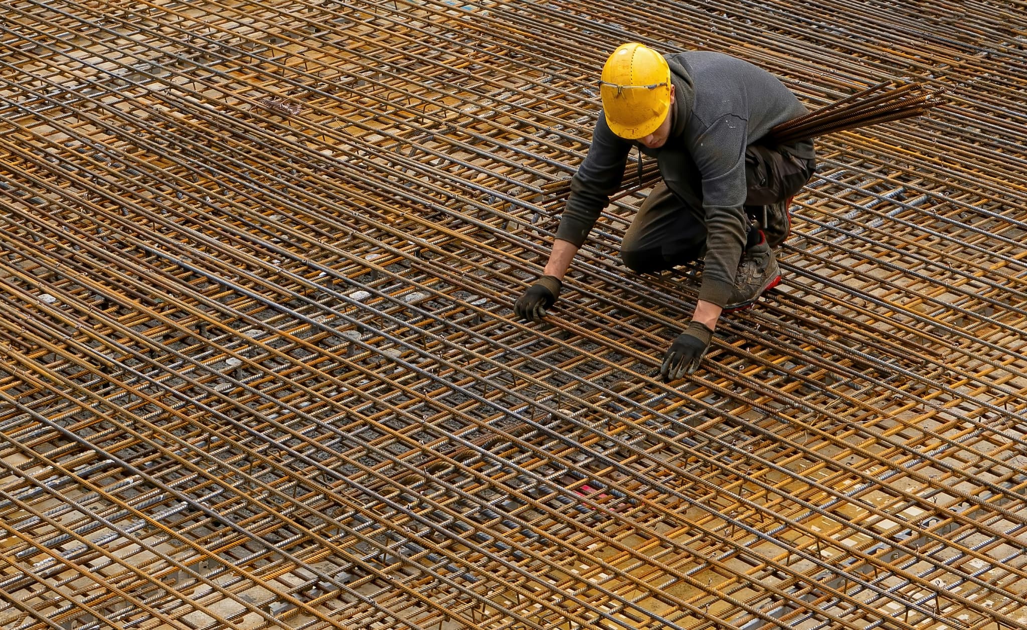 A worker in a hard hat crossing a wide grid of laid rebar