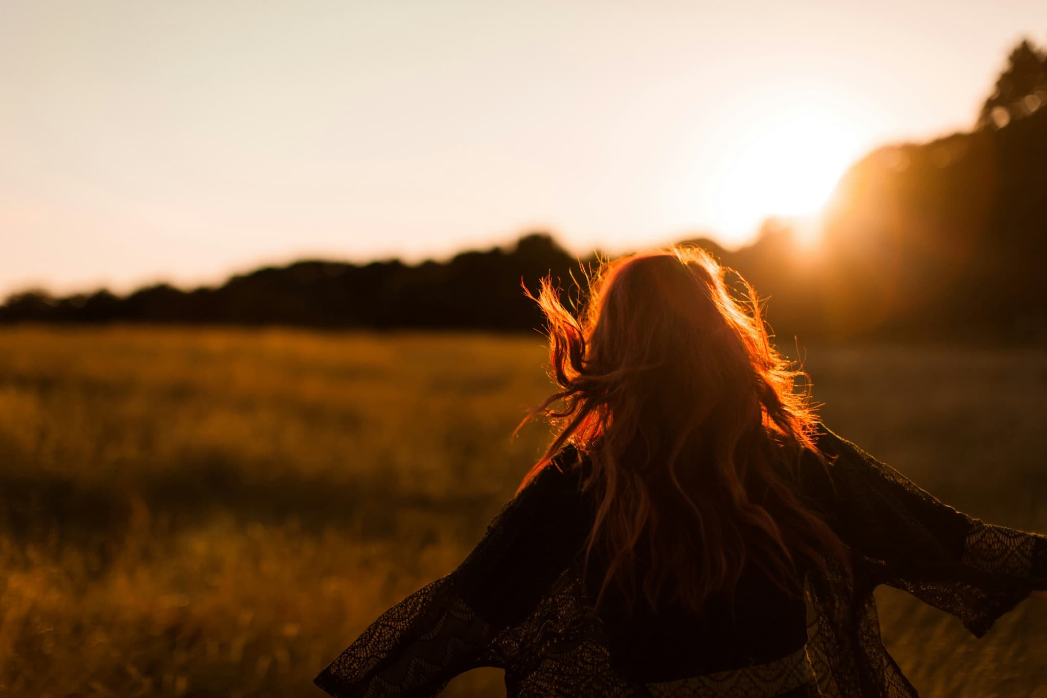 A woman standing in tall grass at golden hour, hair lifting in the wind
